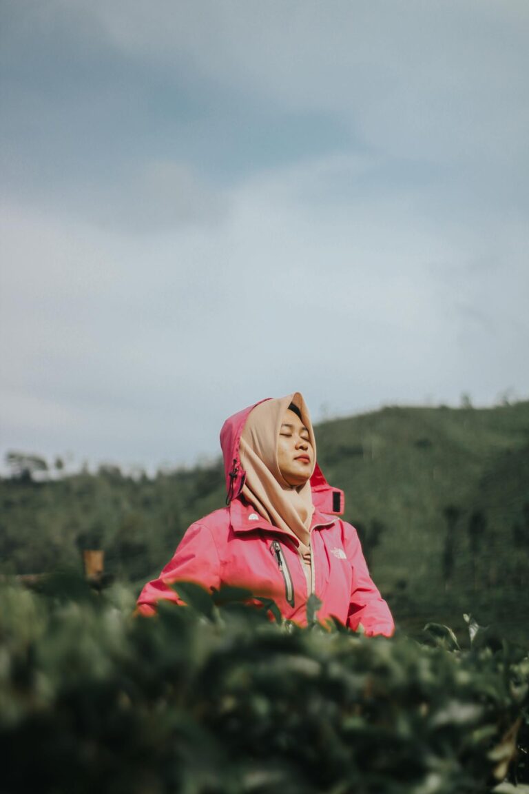 A woman in a hijab and pink jacket enjoys the serene outdoors in Indonesia.